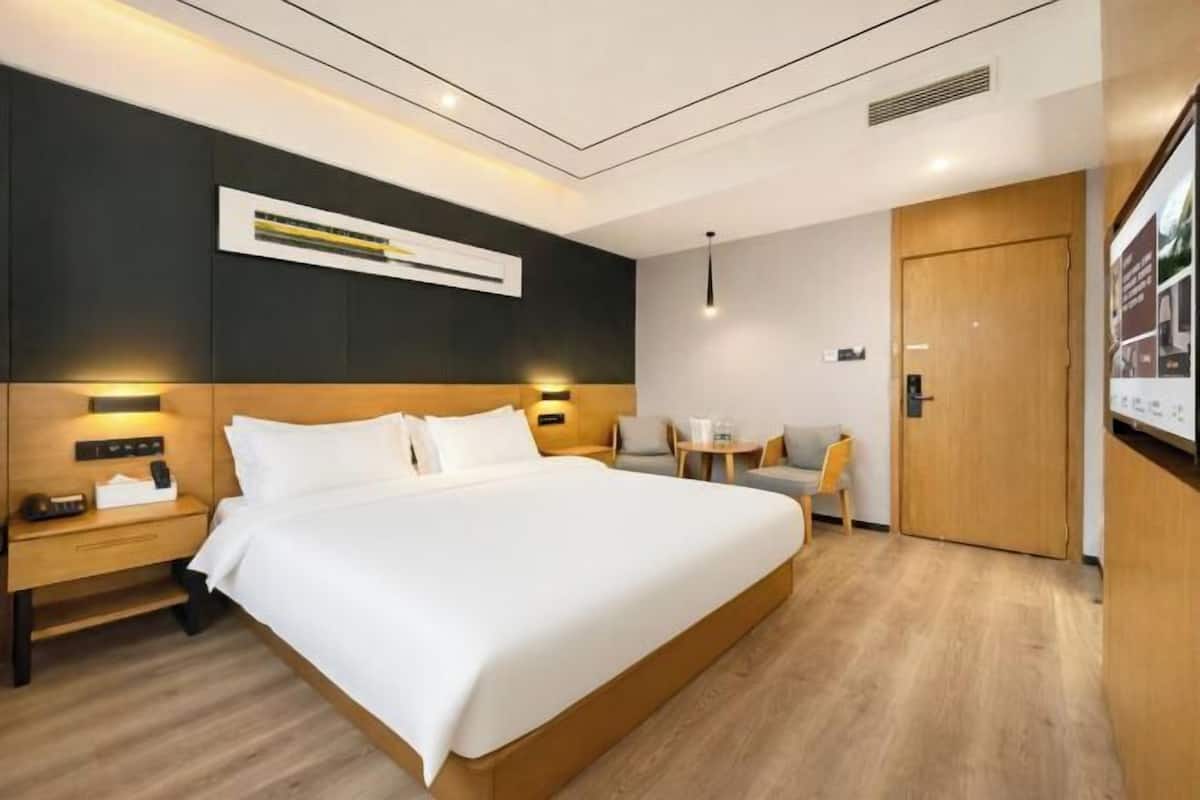 A hotel room with a large bed, bedside tables, a desk, a chair, and a door.