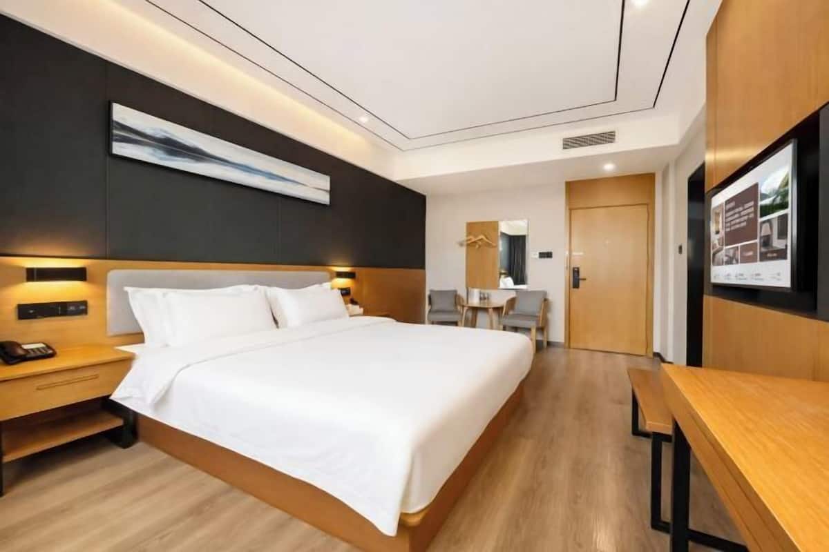 A modern hotel room with a large bed, bedside tables, a desk, and a seating area.