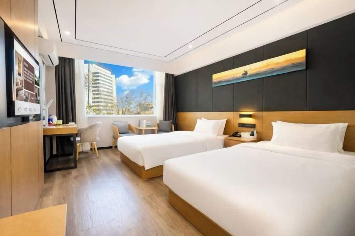 A hotel room with two beds, a desk, and a window with a view of a building.