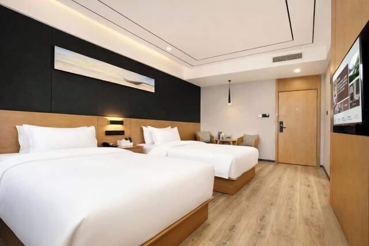 A hotel room with two beds, a desk, a chair, a TV, and a door.
