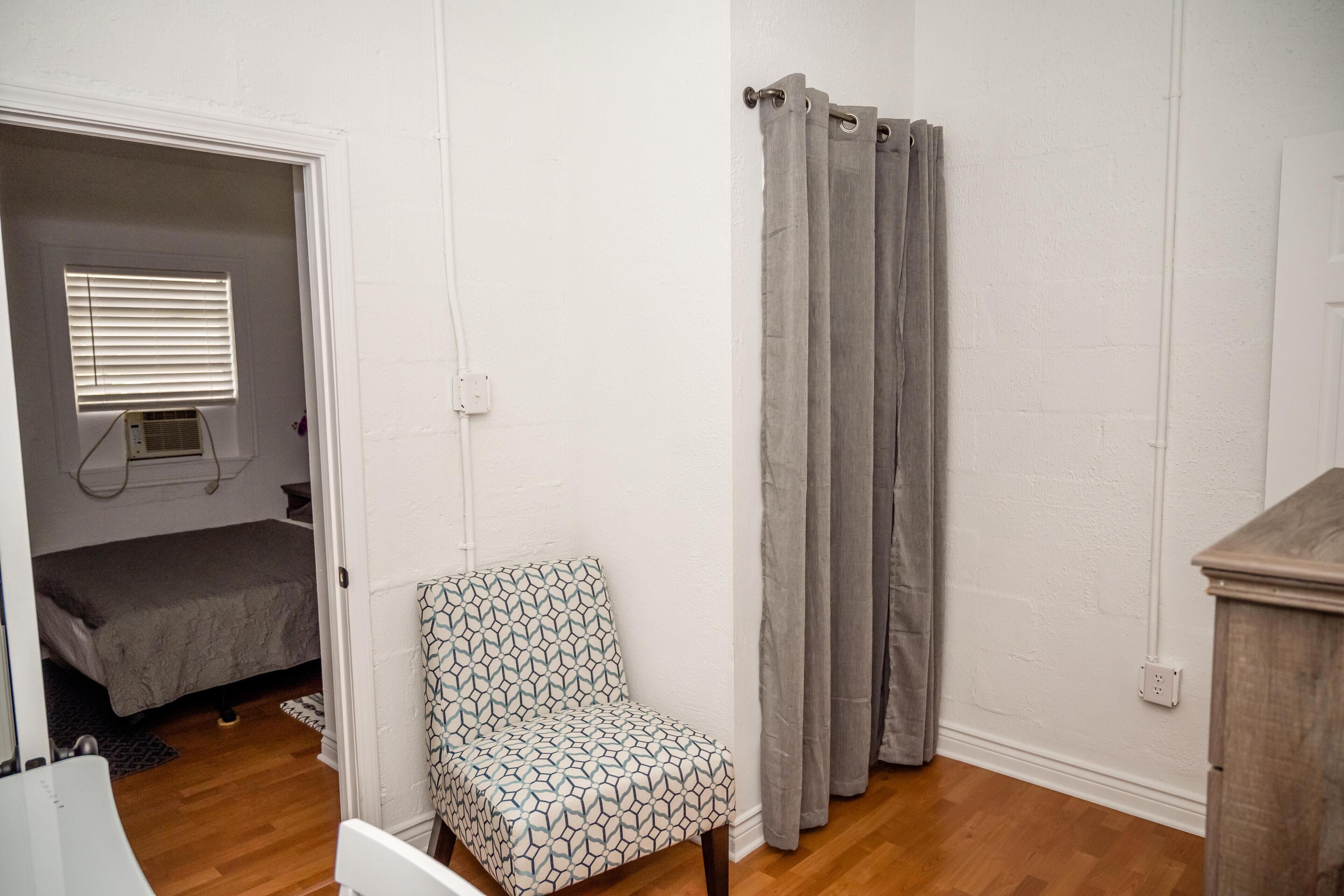 A bedroom with a bed, a chair, a shower curtain, and a wooden cabinet.
