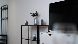 Une pièce moderne avec un meuble TV en métal noir, un meuble blanc et une petite plante posée sur le meuble.