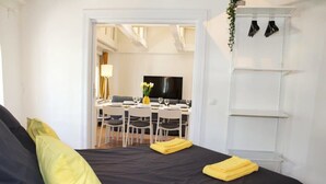 A bedroom with a black bed, yellow pillows, a dining area with a TV, and a white wardrobe.