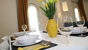 A dining table set with white plates, bowls, cutlery, and a yellow vase with flowers.