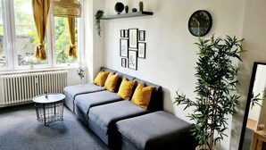 Ein modernes Wohnzimmer mit grauem Sofa, gelben Kissen, einem runden Couchtisch und einer großen Pflanze in einem Topf.