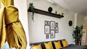 Ein modernes Schlafzimmer mit einer grauen Schlafcouch, gelben Kissen und einer Wand mit gerahmten Bildern.