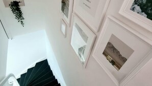 Eine Treppe mit einer weißen Wand und gerahmten Bildern, darunter eines mit dem Schriftzug "TAKE ME TO THE OCEAN WHERE HAPPINESS COMES IN WAVES".