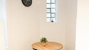 Un pequeño comedor con una mesa redonda de madera, cuatro sillas negras, una planta pequeña en maceta y un reloj de pared.