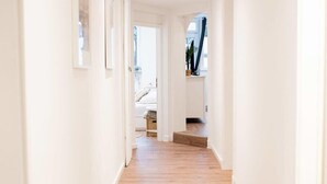 Un pasillo con piso de madera y paredes blancas que conduce a una escalera y una habitación con cama.