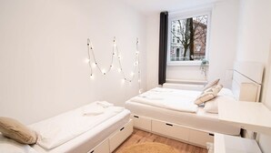 Un dormitorio moderno con dos camas, un ventanal con vistas a edificios y un aplique de pared.