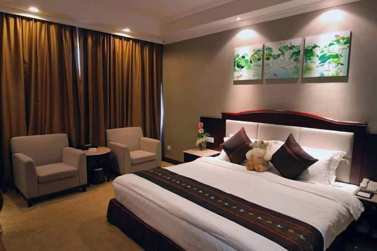 Hotelkamer met een groot bed, twee fauteuils, een kleine tafel en een nachtkastje met lamp.