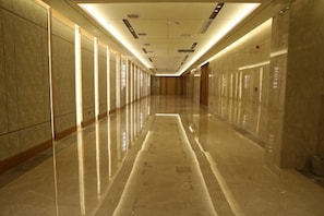 Um corredor longo e bem iluminado, com pisos refletivos e portas em ambos os lados.