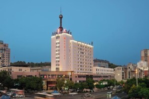 Un hôtel à plusieurs étages, doté d’une tour imposante et d’une plateforme d’observation en forme de sphère, entouré d’autres bâtiments et bordé par une rue animée.