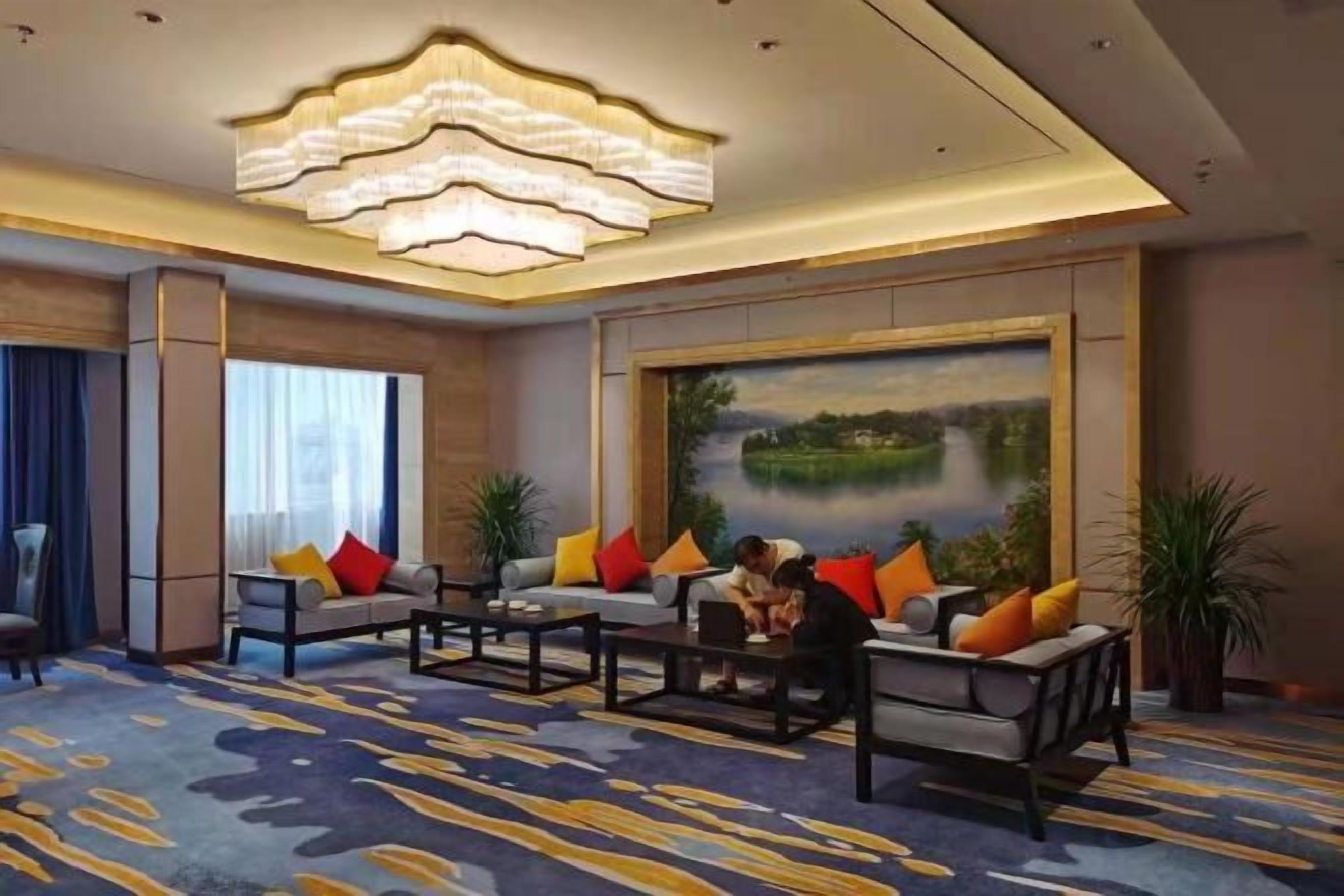 A hotel lobby with a large painting, a chandelier, and a seating area with multiple sofas and a coffee table.