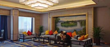 A hotel lobby with a large painting, a chandelier, and a seating area with multiple sofas and a coffee table.