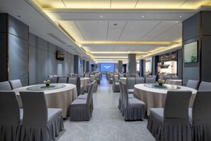 Une salle de conférence d’hôtel avec des tables et des chaises rondes, un grand écran à l’avant et un aménagement intérieur moderne.