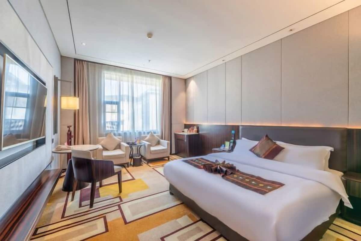 Een moderne hotelkamer met een groot bed, een zithoek met stoelen, een kleine tafel en een televisie.