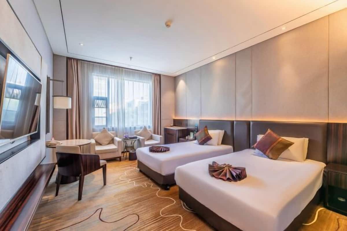Een hotelkamer met twee bedden, een bureau, een stoel, een televisie en een groot raam.