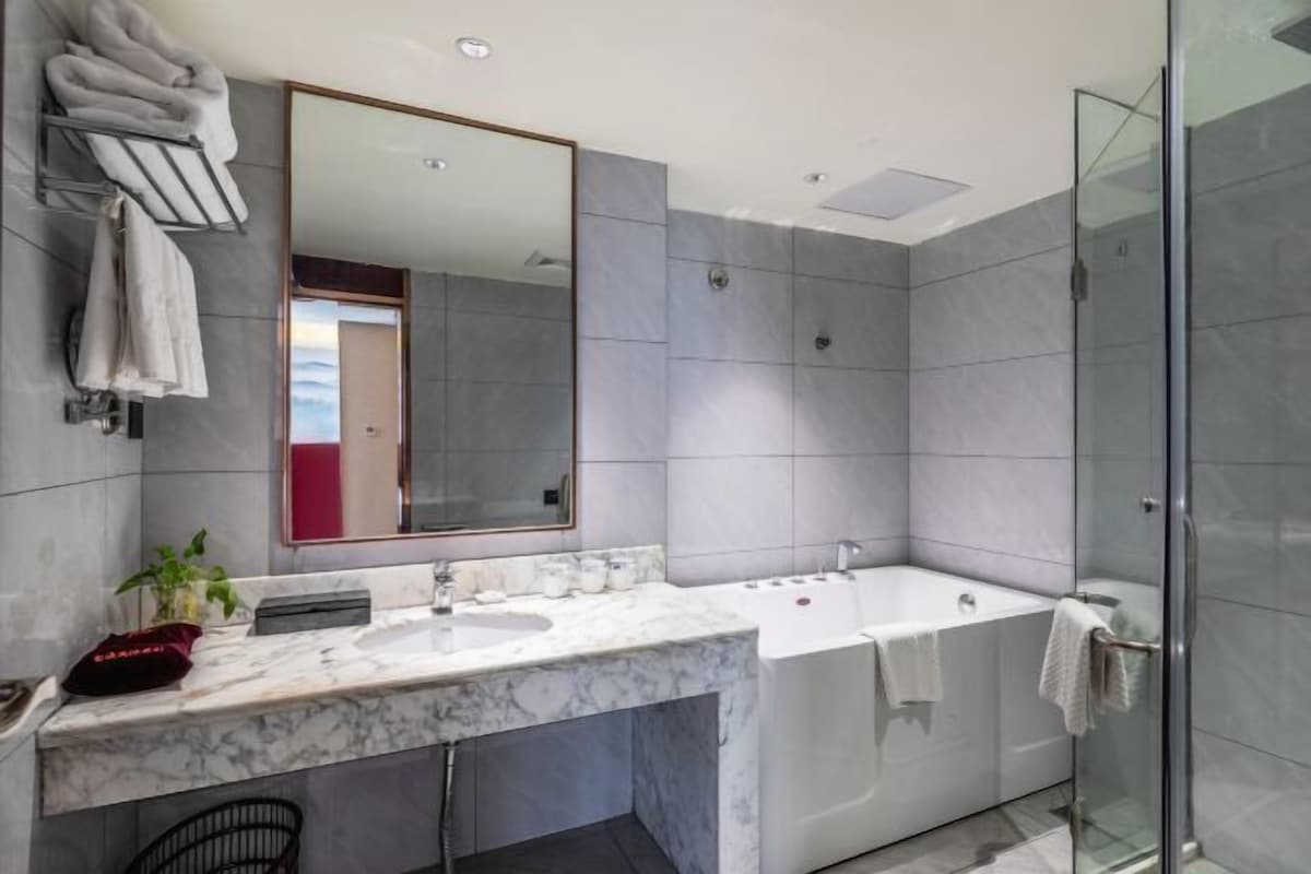 Een moderne badkamer met een marmeren wastafel, een grote spiegel, een douchecabine van glas en een ingebouwd bad.