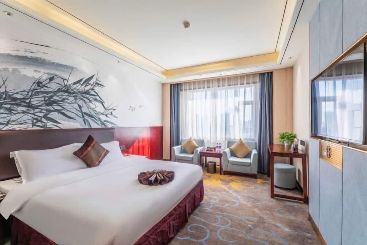 Een hotelkamer met een groot bed, twee fauteuils, een tafeltje en een televisie.