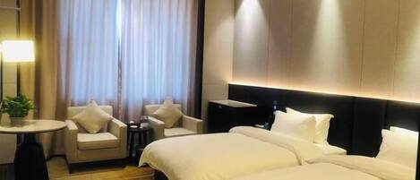 A hotel room with a large bed, two armchairs, a small table, and a large window with curtains.