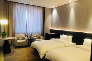 Ein Hotelzimmer mit einem großen Bett, zwei Sesseln, einem kleinen Tisch und einem großen Fenster mit Vorhängen.