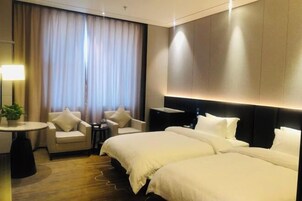 Habitación de hotel con una cama grande, dos sillones, una mesita y un ventanal con cortinas.