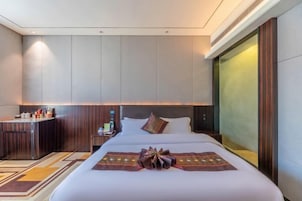 A hotel room with a large bed, a small desk, a minibar, and a large window.
