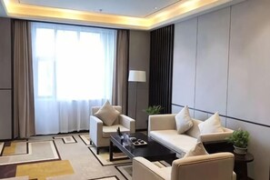 Una habitación de hotel moderna con sofá, sillones, una mesita de centro y un gran ventanal con cortinas.