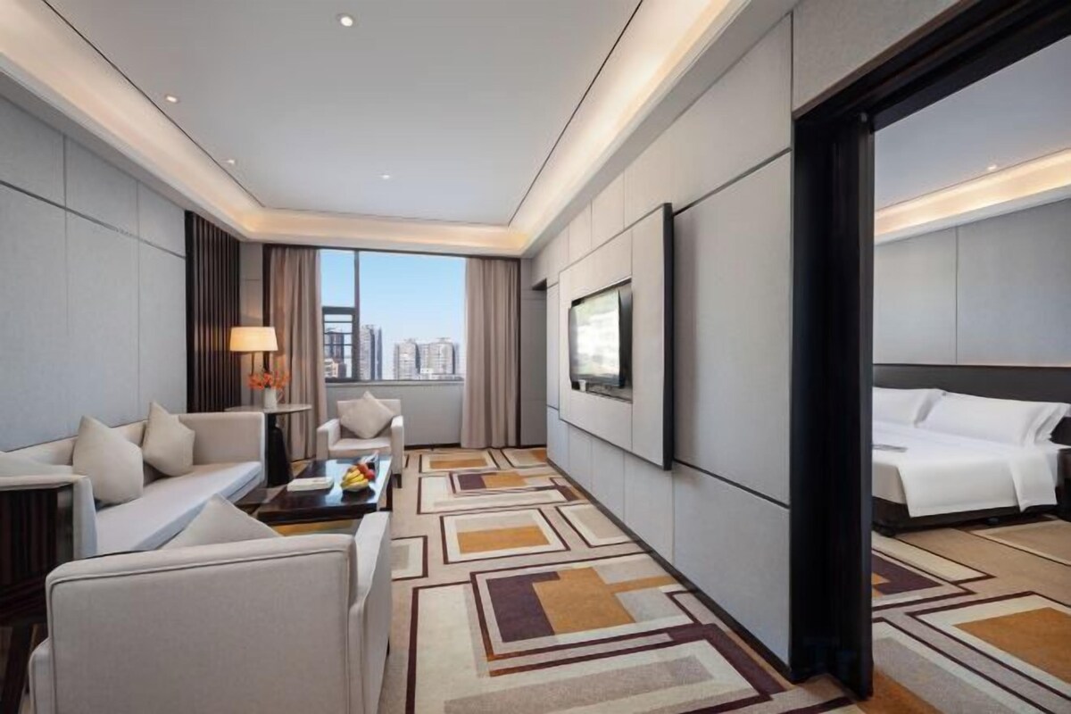 Ein Hotelzimmer mit Sofa, Couchtisch, Fernseher, Bett und Blick auf die Stadt.