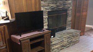 Ein Wohnzimmer mit Kamin aus Stein, einer Holzunterhaltungsecke und einem Fernseher.