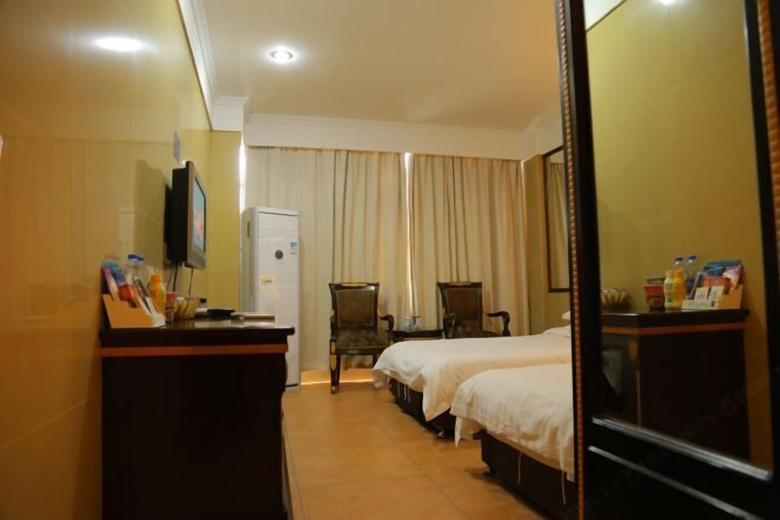 A hotel room with two beds, a desk, a chair, a television, and a minibar.