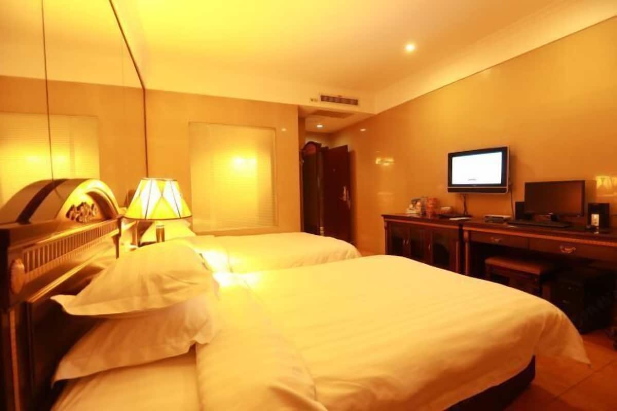 A hotel room with two beds, a television, a desk, and a lamp.