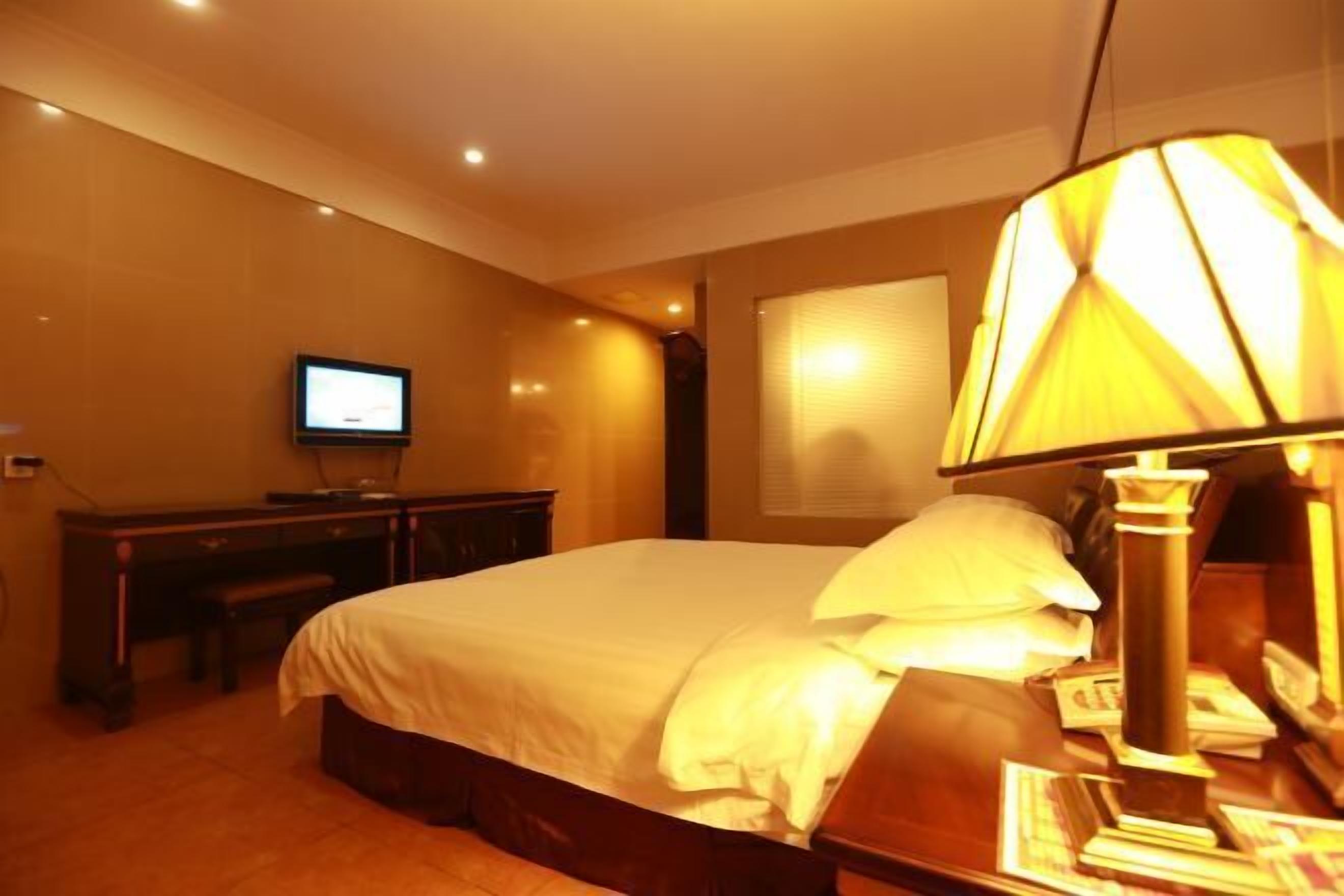 A hotel room with a bed, a desk, a television, and a lamp.