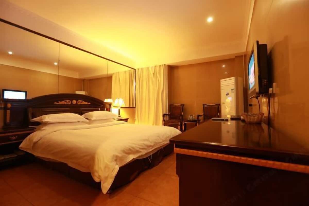 A hotel room with a bed, a desk, a chair, a television, and a mirror.