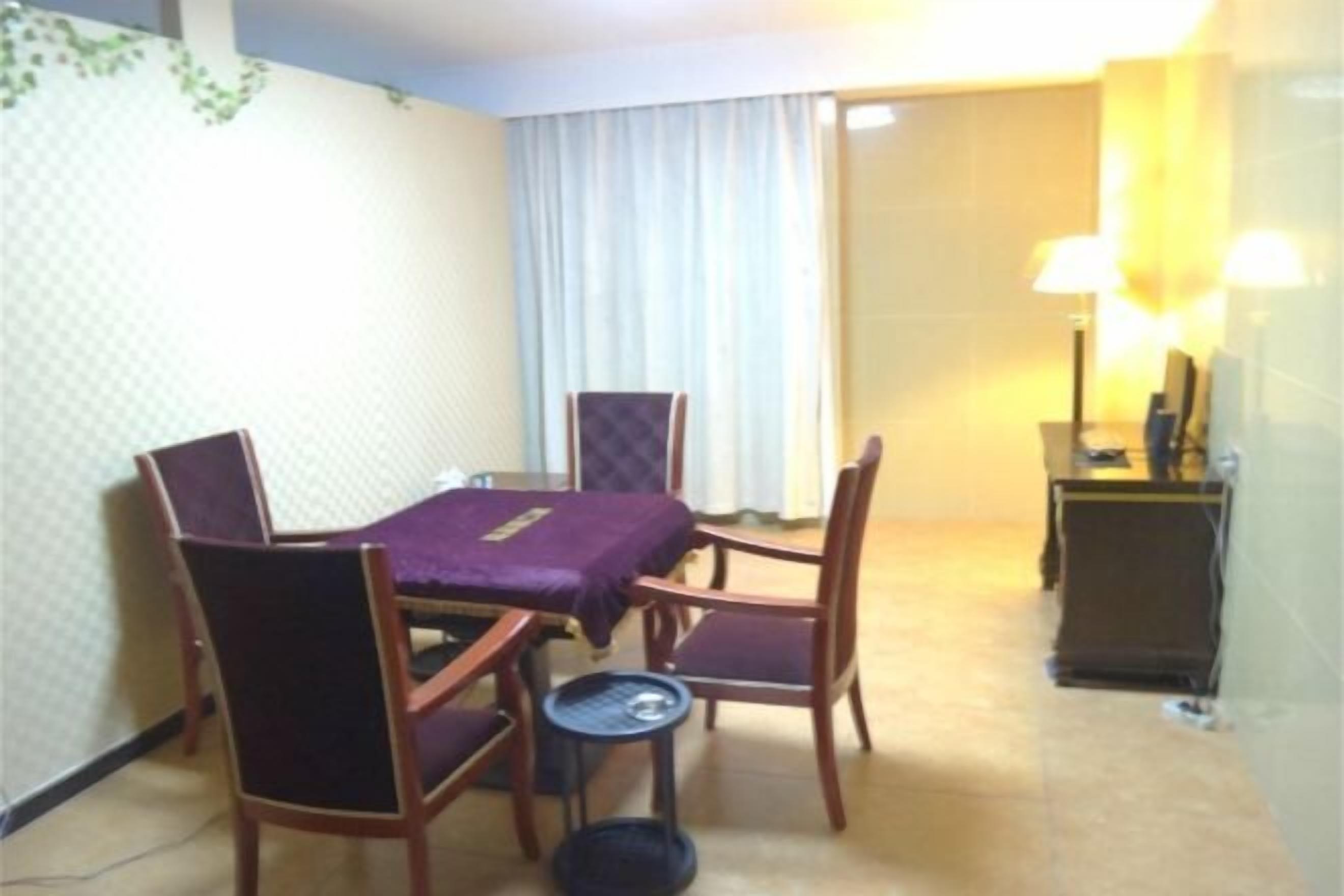 A hotel room with a dining table, four chairs, a small side table, a lamp, and a mirror.