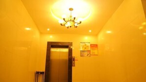 A brightly lit elevator area with a chandelier, a closed elevator door, and a small table with a chair. - Laike Yangming Hotel (Chizhou)
