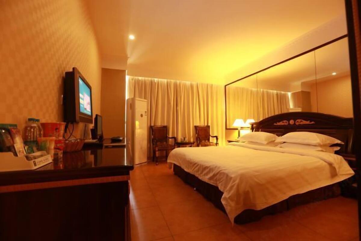 A hotel room with a bed, a desk with a television, a chair, and a door.