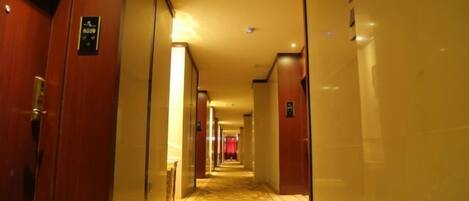A hotel corridor with wooden doors, a patterned carpet, and a warm lighting ambiance.