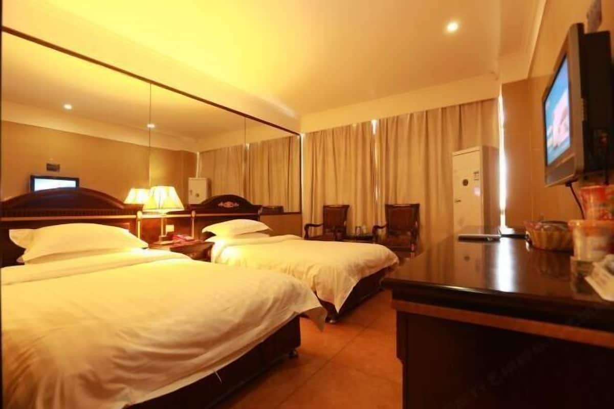 A hotel room with two beds, a desk, a television, and a mirror.