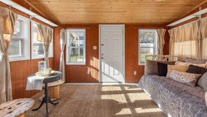 A cozy room with a wooden ceiling, a bed with patterned bedding, a small table with a lamp, and curtains on the windows.