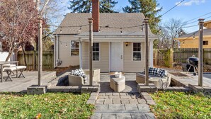A small house with a brick chimney, a front porch with wicker furniture, and a backyard with a grill.