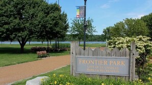 A park sign with a path, benches, and a lamp post.