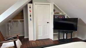 Une pièce avec un lit, un téléviseur posé sur un meuble, une porte blanche et une chaise en bois.