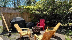 Une terrasse extérieure avec une plateforme en bois, un foyer et quatre fauteuils Adirondack.