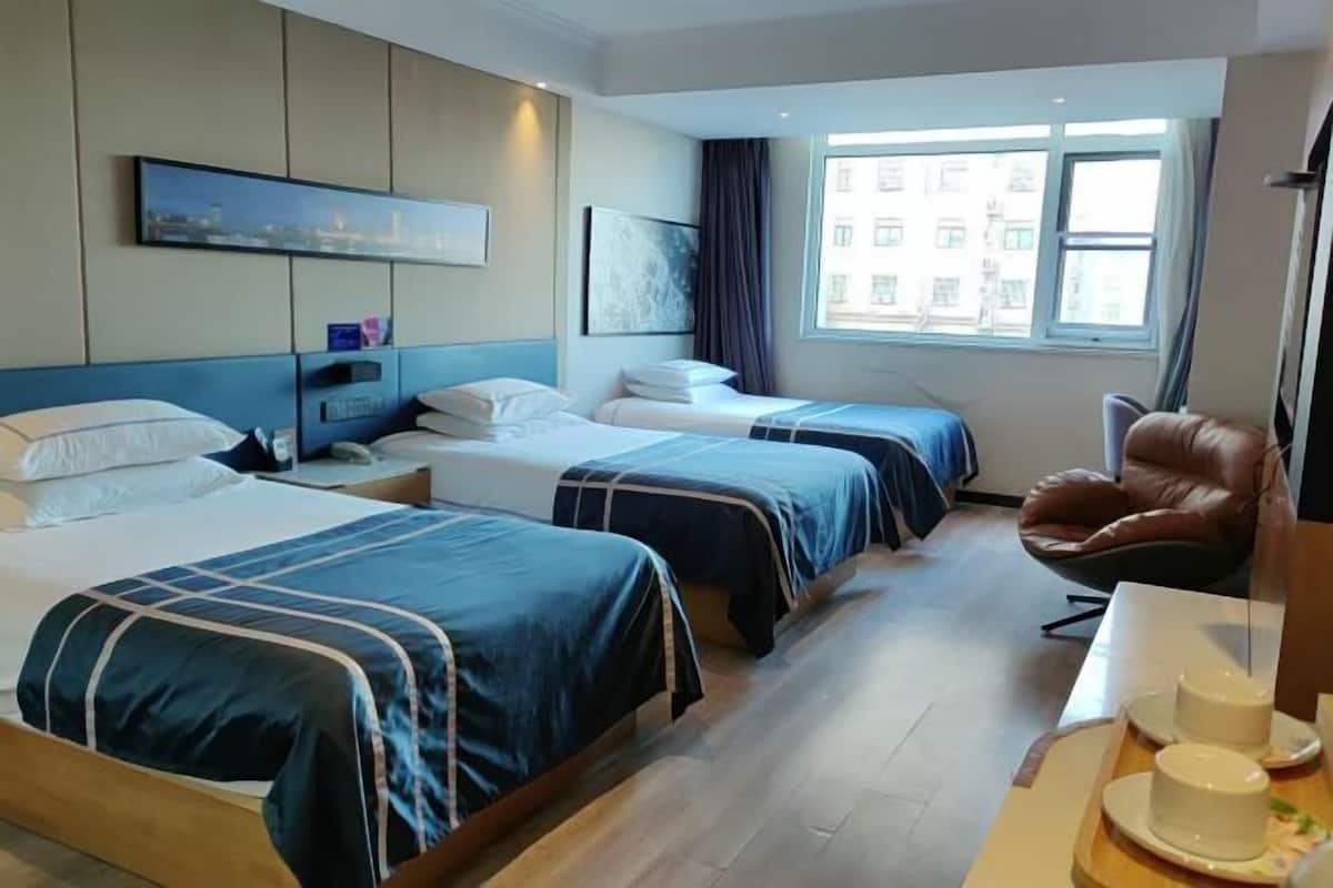 A hotel room with two beds, a desk, a chair, and a window with a city view.