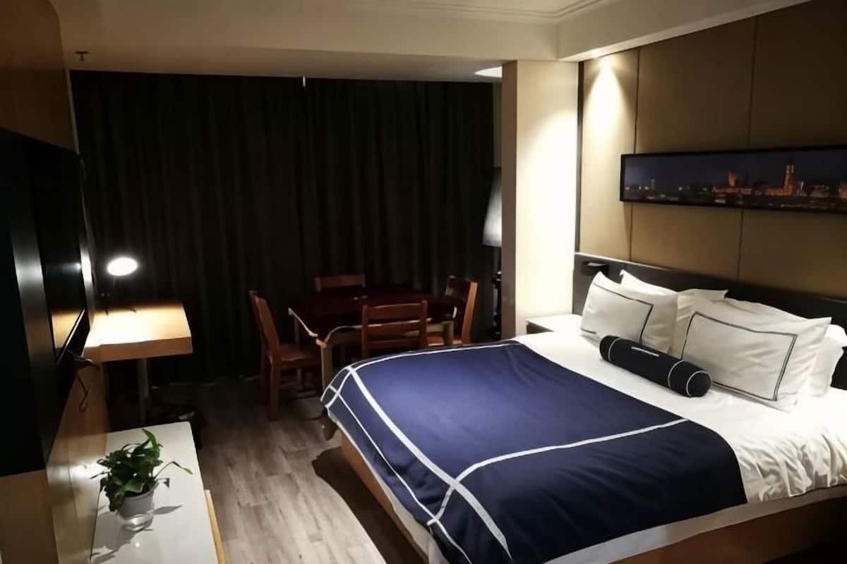 A hotel room with a bed, a desk, a chair, a TV, and a painting on the wall.