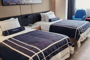 Twin beds with matching headboards, a flat-screen TV mounted on the wall, and a blue chair by the window.