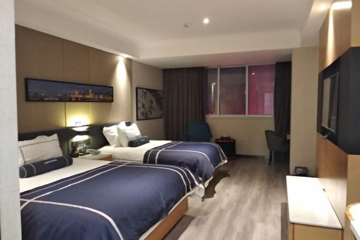 A hotel room with two beds, a desk, a chair, a TV, and a window with curtains.