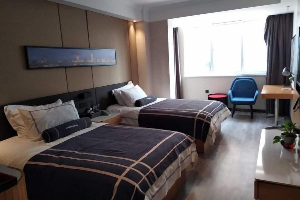 A hotel room with two beds, a desk, a chair, a nightstand, and a window with curtains.